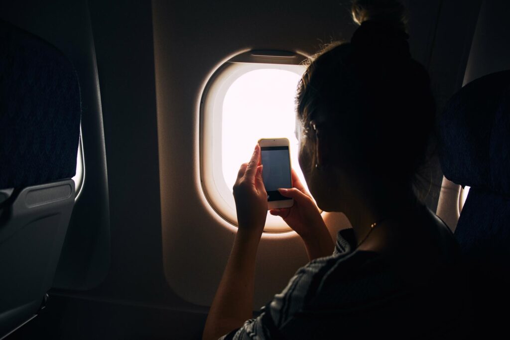 Donna in aereo riprende il panorama con il telefono dal finestrino